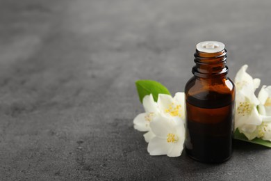 Photo of Essential oil and jasmine flowers on grey table. Space for text