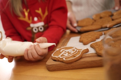 Photo of Little girl decorating tasty Christmas cookie at wooden table, closeup
