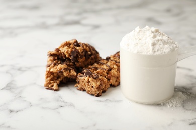 Photo of Tasty protein bars and scoop of powder on marble table