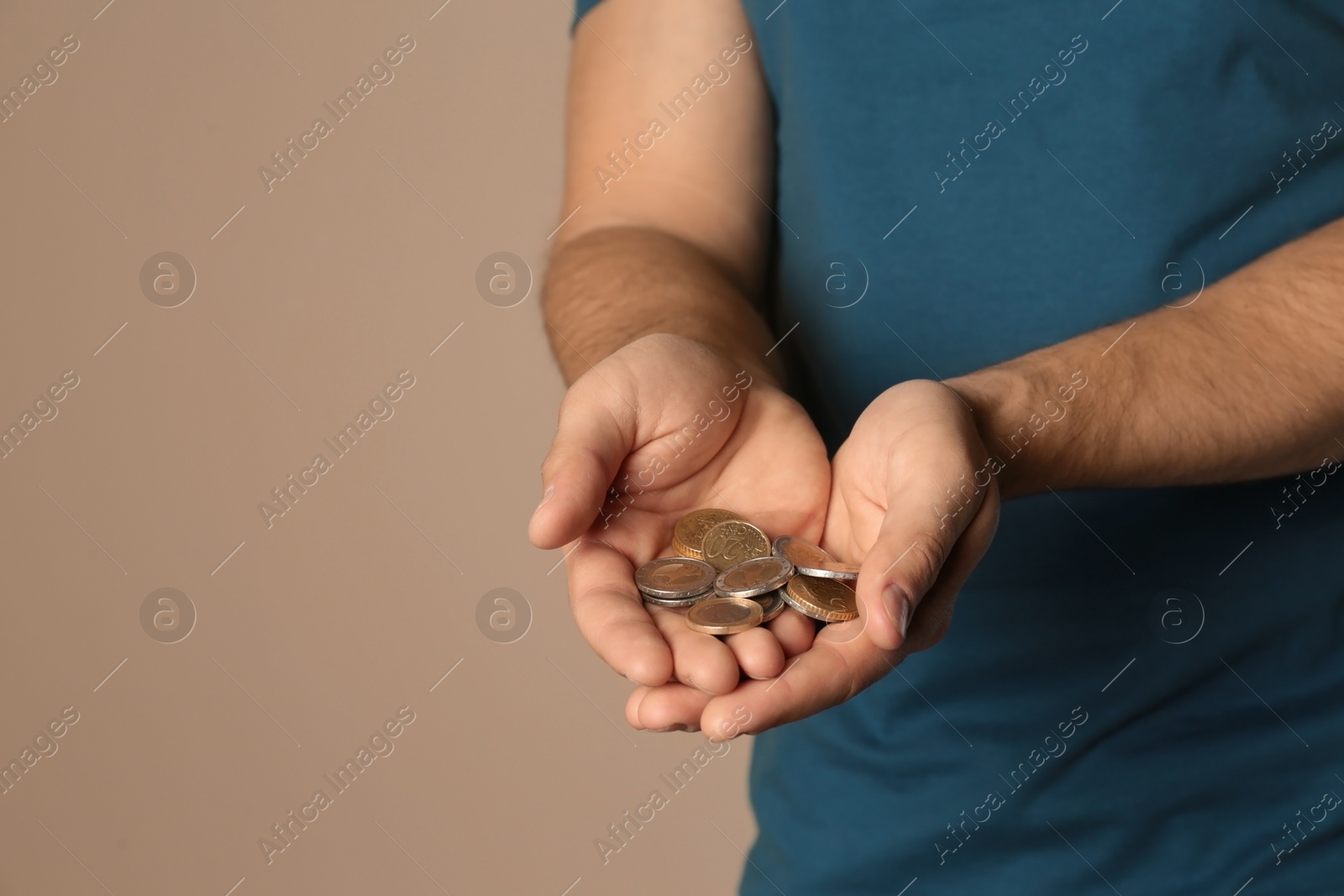Photo of Young man with handful of coins on beige background, closeup. Space for text