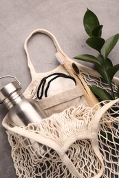 Fishnet bag with different items and green twig on grey table, top view. Conscious consumption