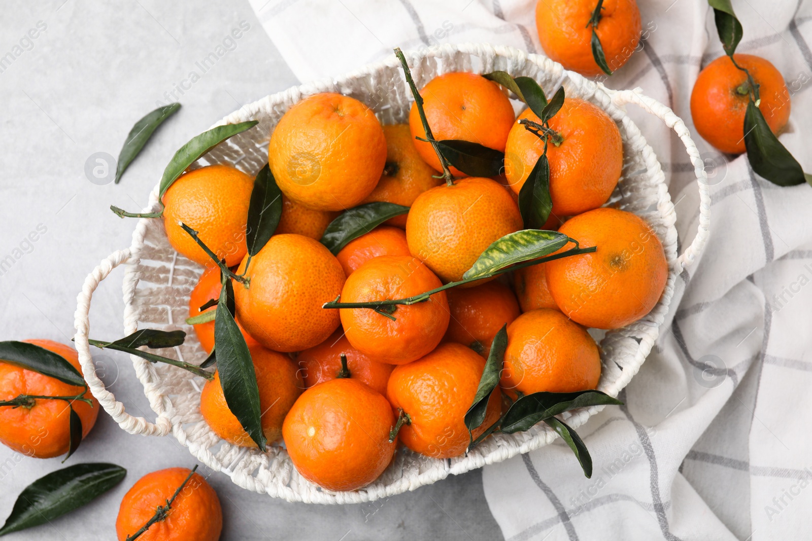 Photo of Basket with fresh ripe tangerines and leaves on grey table, flat lay