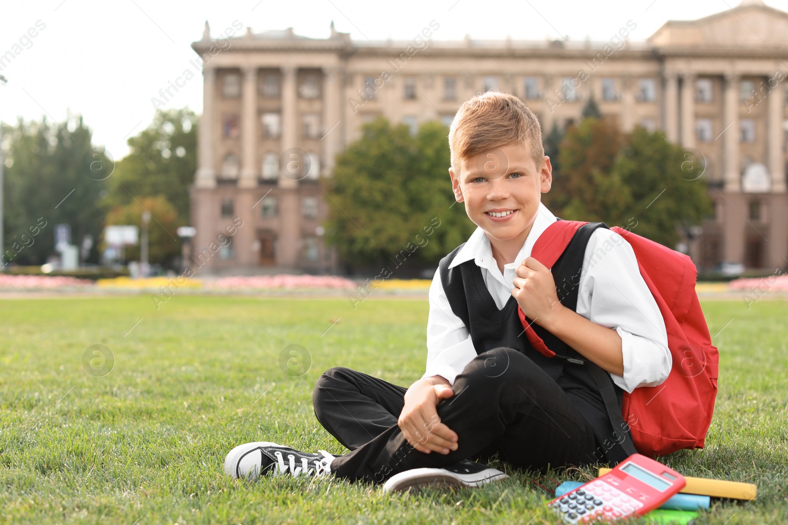 Photo of Schoolboy with stationery sitting on grass outdoors