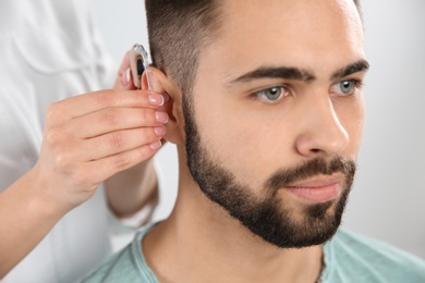 Photo of Otolaryngologist putting hearing aid in man's ear on white background