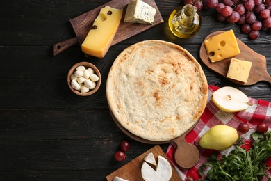 Flat lay composition with pizza crust and fresh ingredients on black wooden table