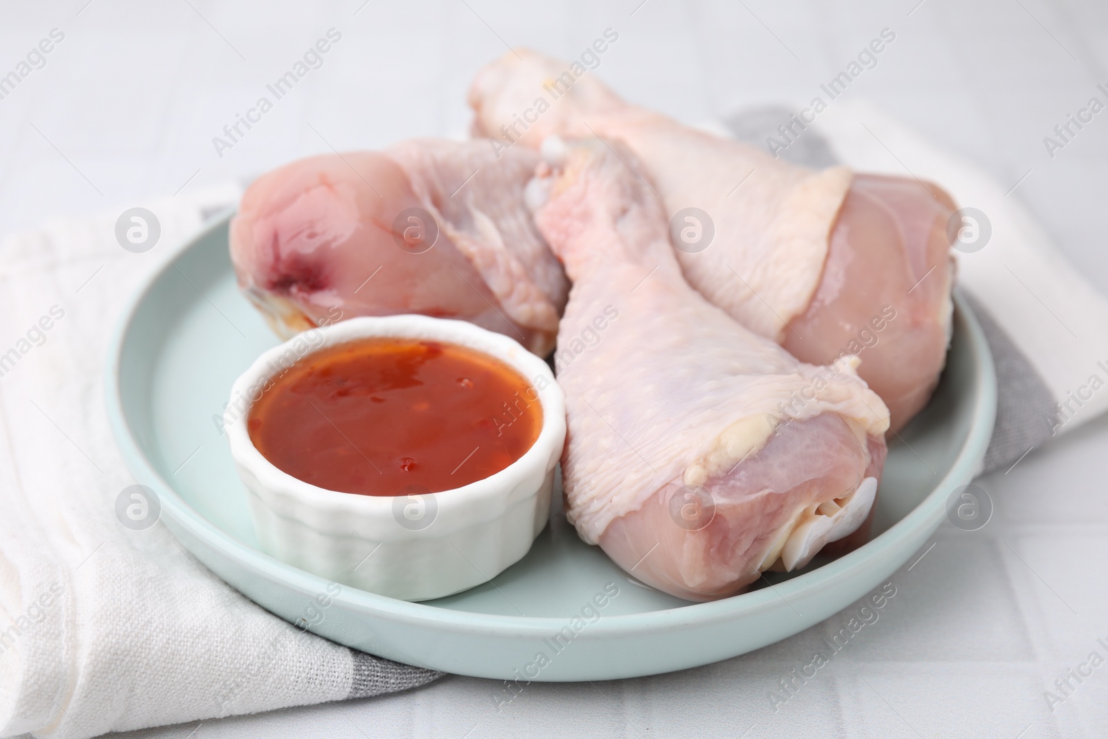 Photo of Fresh marinade and raw chicken drumsticks on white tiled table, closeup