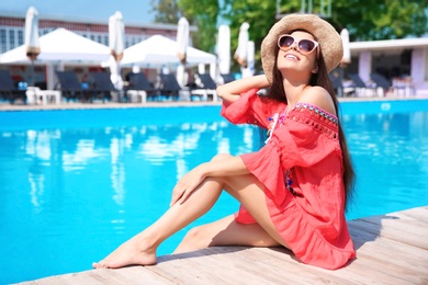 Photo of Beautiful young woman sitting near outdoor swimming pool