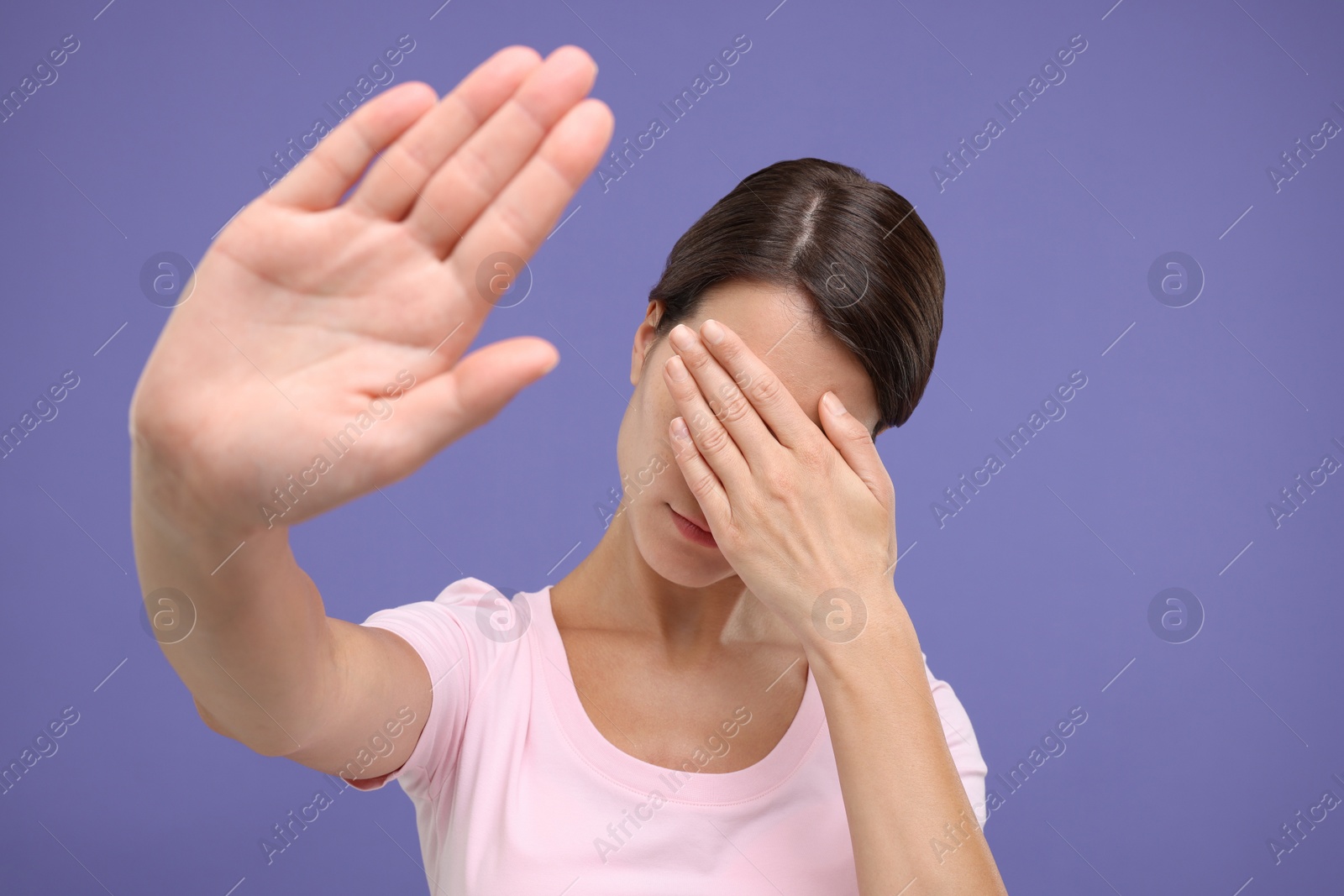 Photo of Embarrassed woman covering face with hand on violet background