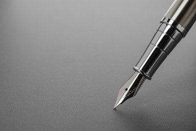 Photo of Stylish silver fountain pen on light grey textured table, closeup. Space for text