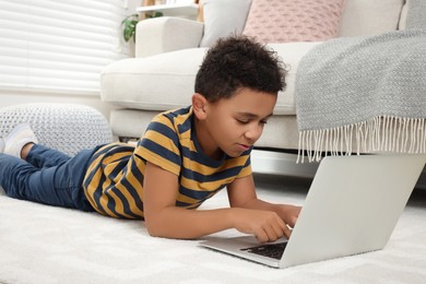 Photo of Cute African-American boy using laptop on floor at home