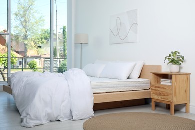 Wooden bed with soft white mattress, blanket and pillows in cozy room interior