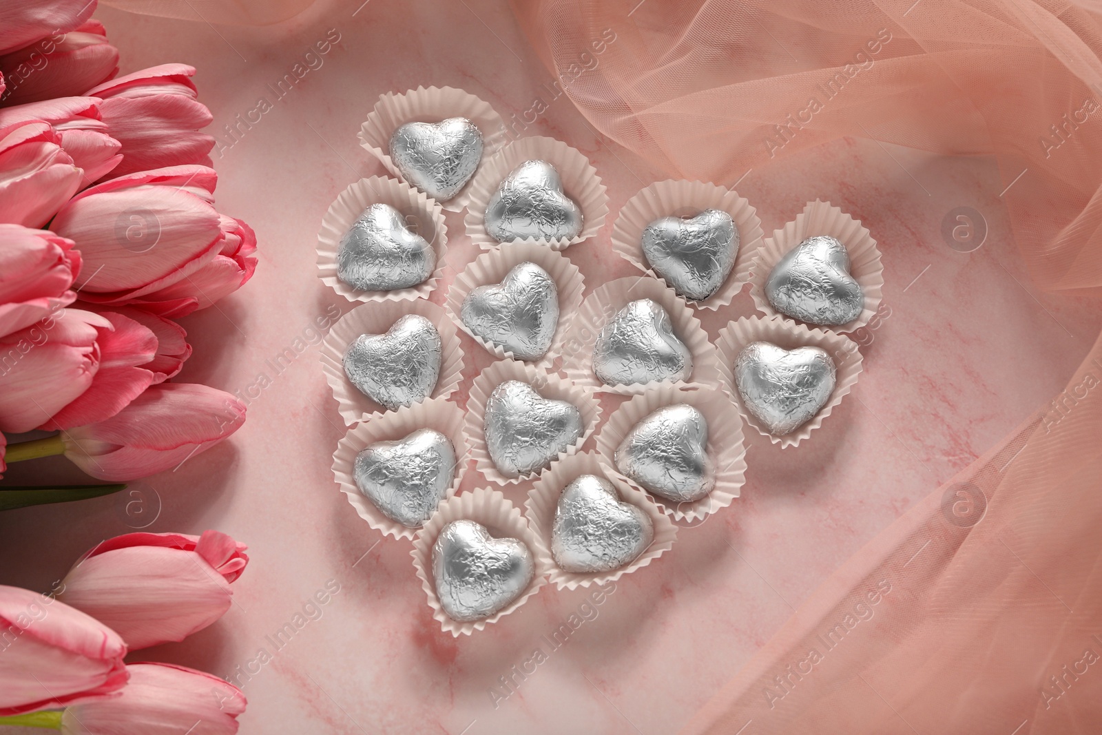 Photo of Heart made with delicious chocolate candies and beautiful tulips on pink table, flat lay. Space for text