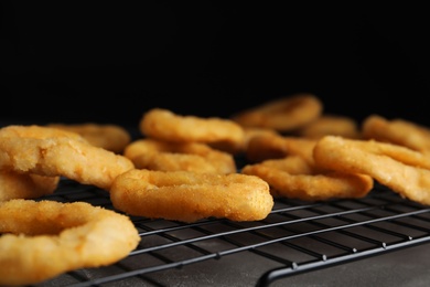 Photo of Cooling rack with fried onion rings on grey table, closeup