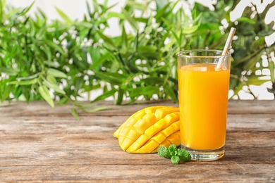 Photo of Fresh mango drink and cut fruit on wooden table against blurred background. Space for text