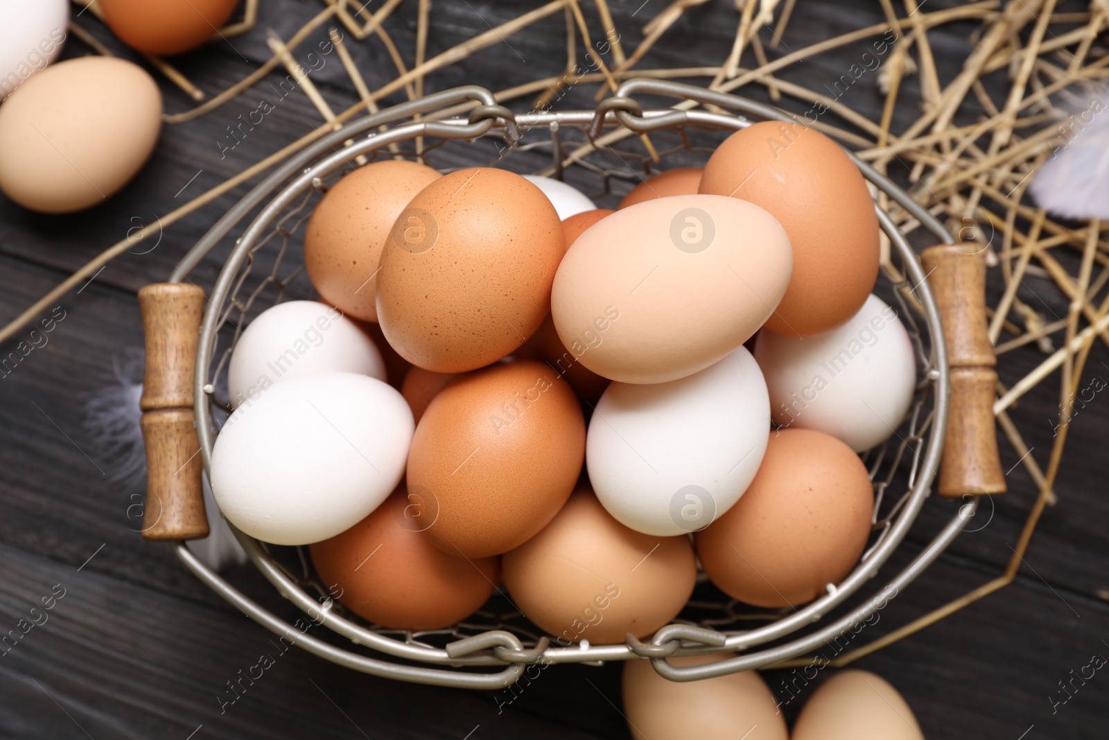 Photo of Fresh chicken eggs and dried straw on black wooden table, flat lay