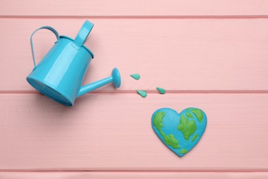 Photo of Happy Earth Day. Flat lay composition with heart shaped plasticine planet and watering can on pink wooden table