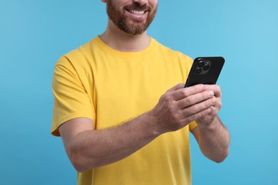 Photo of Smiling man using smartphone on light blue background, closeup