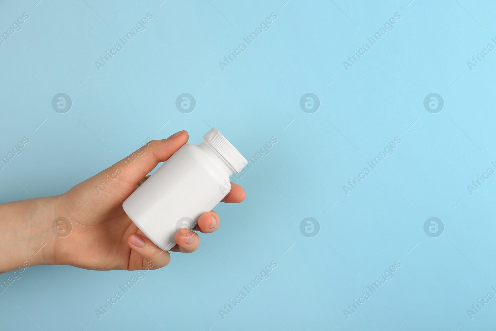 Photo of Woman holding blank white jar of vitamins on light blue background, closeup. Space for text