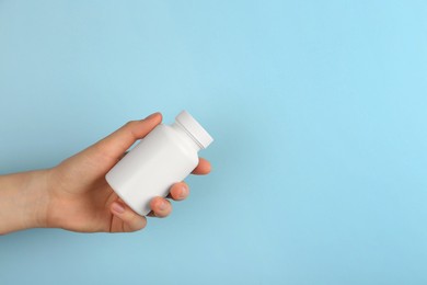 Woman holding blank white jar of vitamins on light blue background, closeup. Space for text