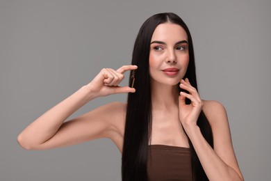 Beautiful young woman holding skincare ampoule on grey background