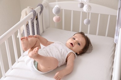 Cute little baby lying in crib with hanging mobile