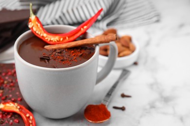 Cup of hot chocolate with chili pepper and cinnamon on white marble table, closeup. Space for text