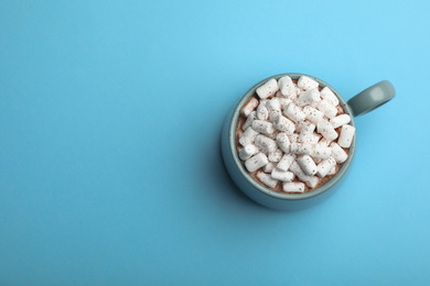 Photo of Delicious cocoa drink with marshmallows on light blue background, top view. Space for text