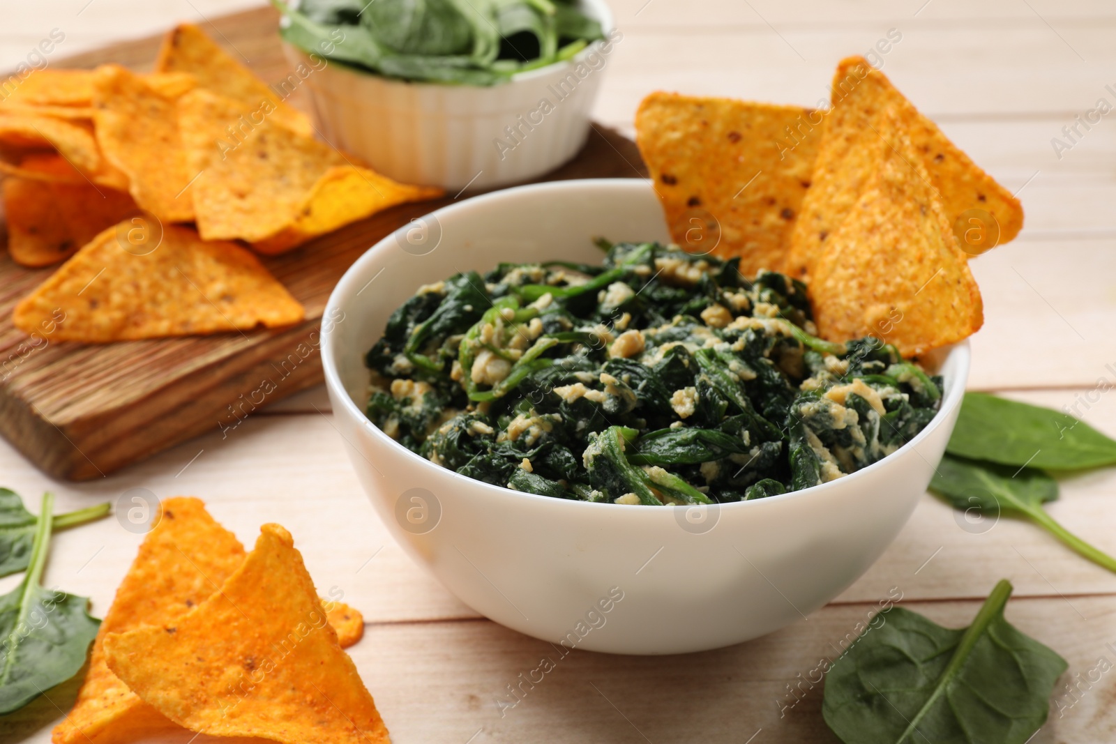 Photo of Tasty spinach dip with eggs in bowl and nachos chips on light wooden table, closeup