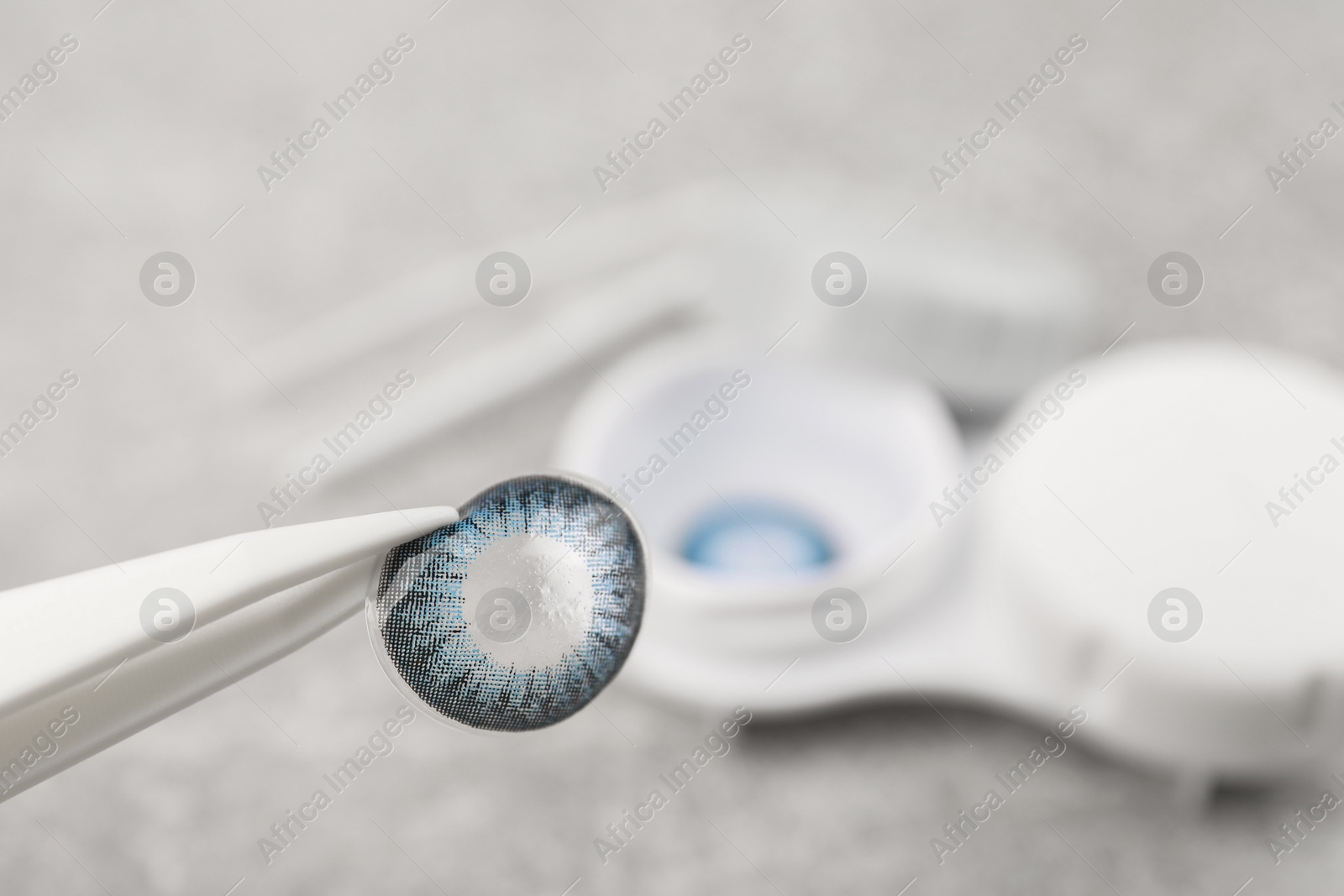 Photo of Tweezers with blue contact lens over table, closeup. Space for text