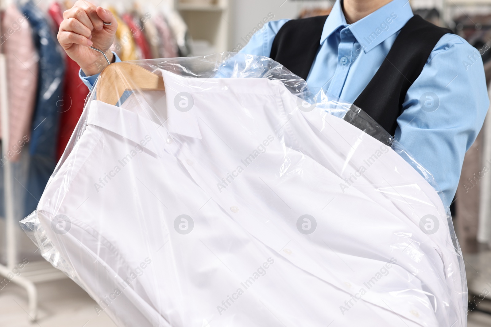 Photo of Dry-cleaning service. Woman holding shirt in plastic bag indoors, closeup