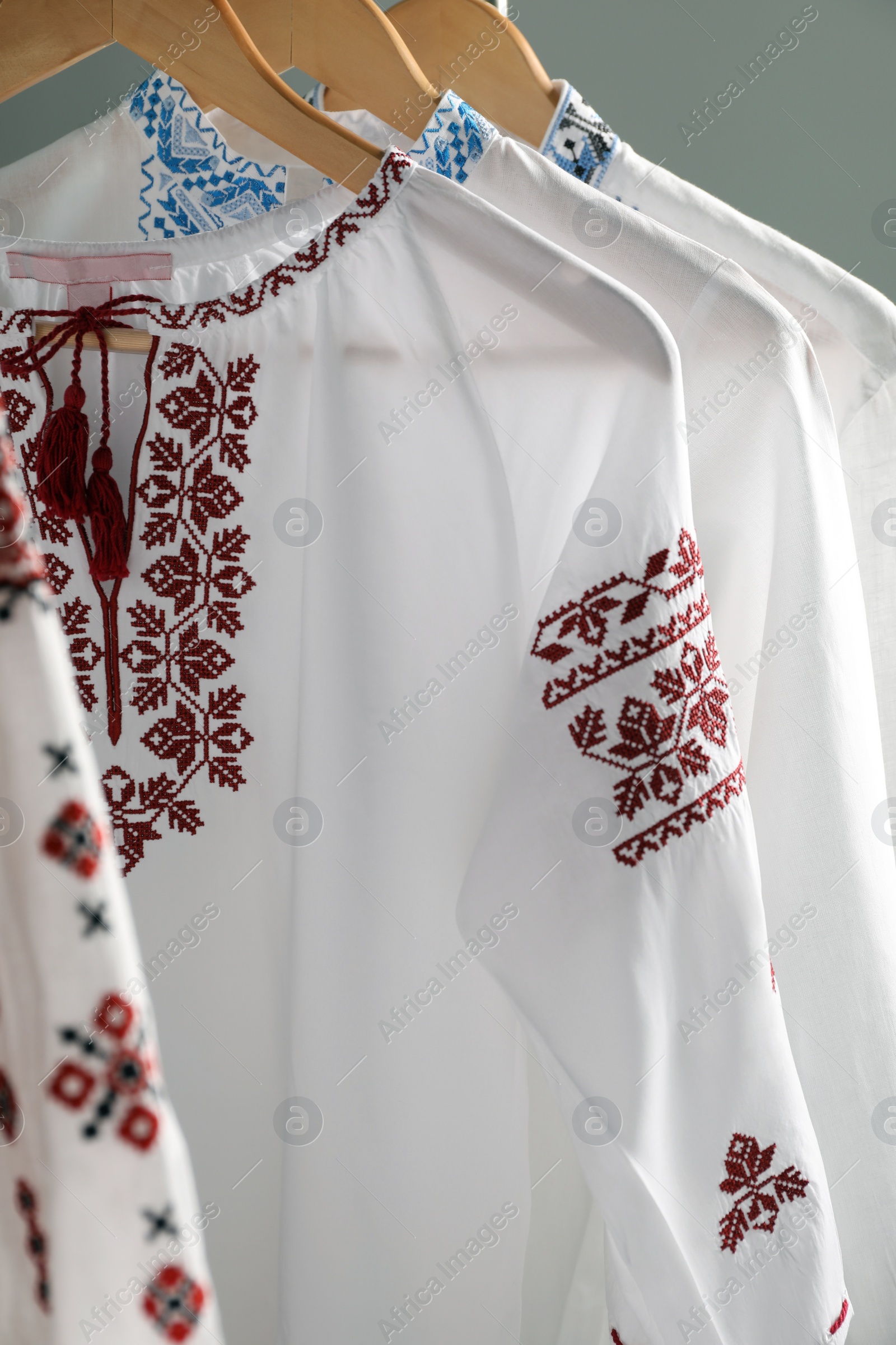 Photo of Beautiful shirts with different embroidery designs hanging on grey background, closeup. Ukrainian national clothes