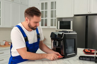 Photo of Repairman with screwdriver fixing coffee machine at table in kitchen