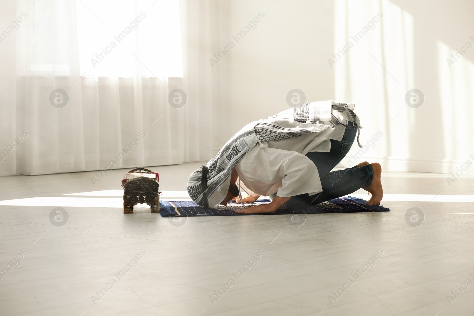 Photo of Muslim man in traditional clothes praying on rug indoors