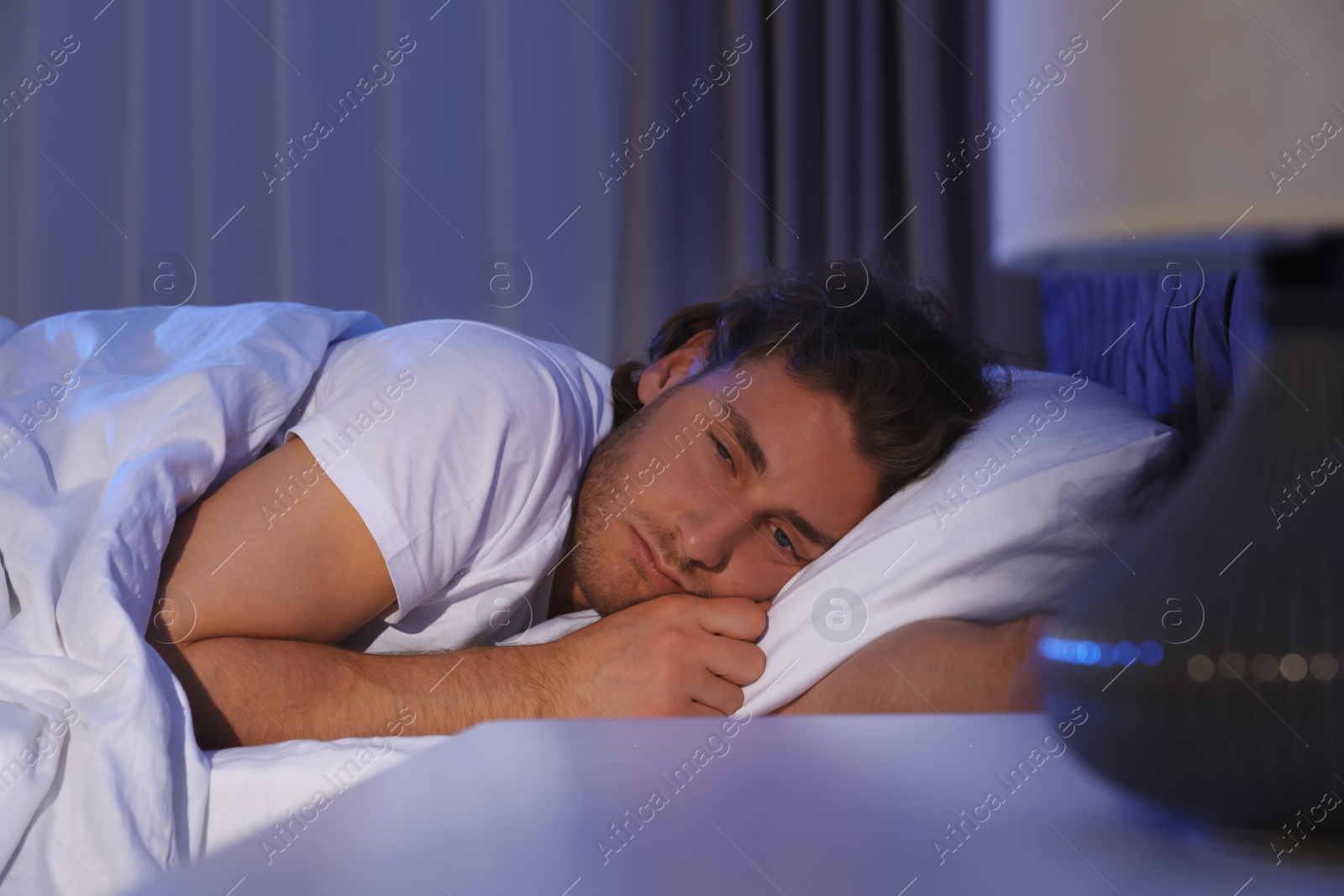 Photo of Sleepy young man lying under blanket at night. Bedtime