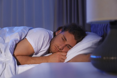 Sleepy young man lying under blanket at night. Bedtime