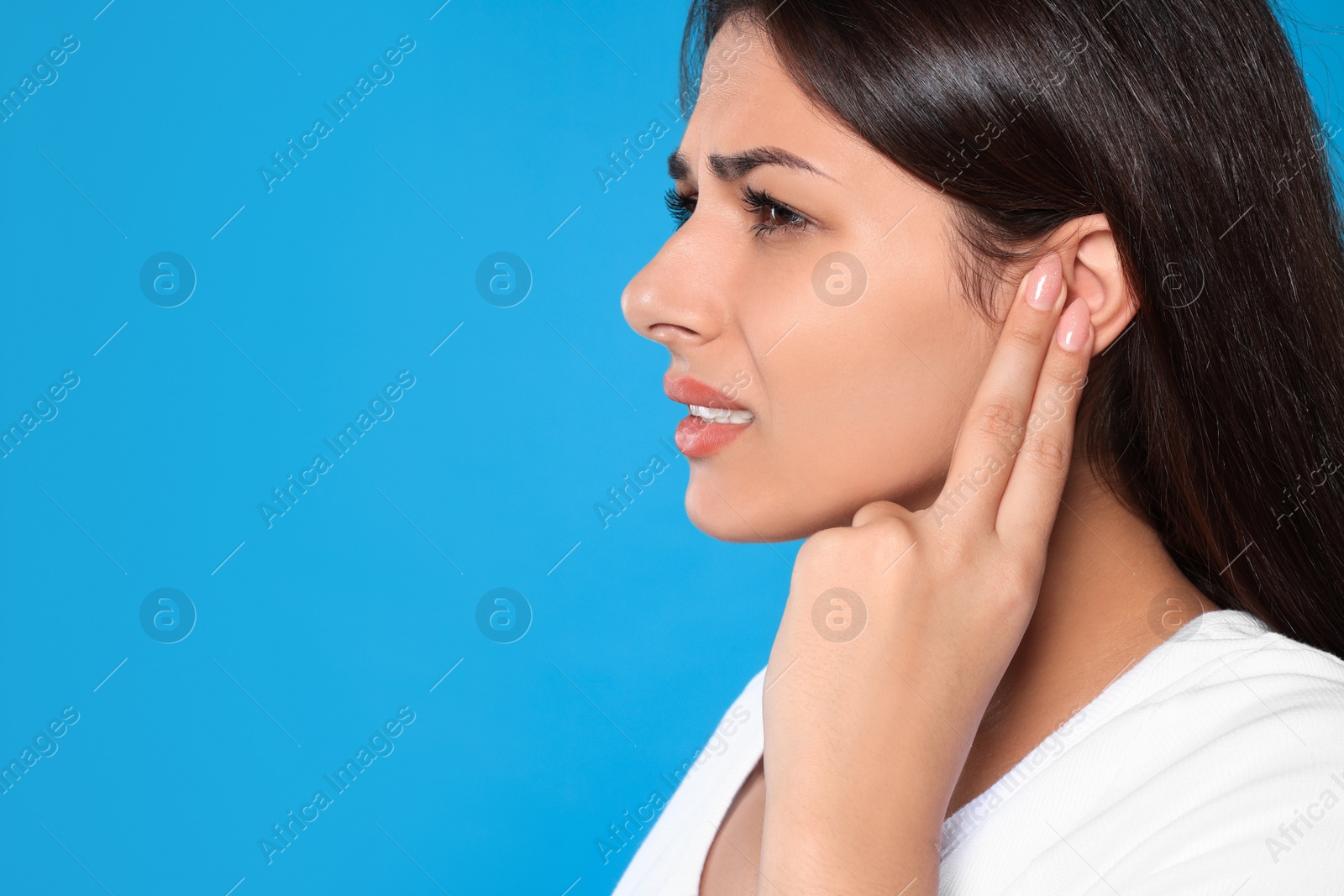 Photo of Young woman suffering from ear pain on light blue background, closeup. Space for text