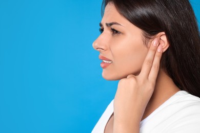 Young woman suffering from ear pain on light blue background, closeup. Space for text