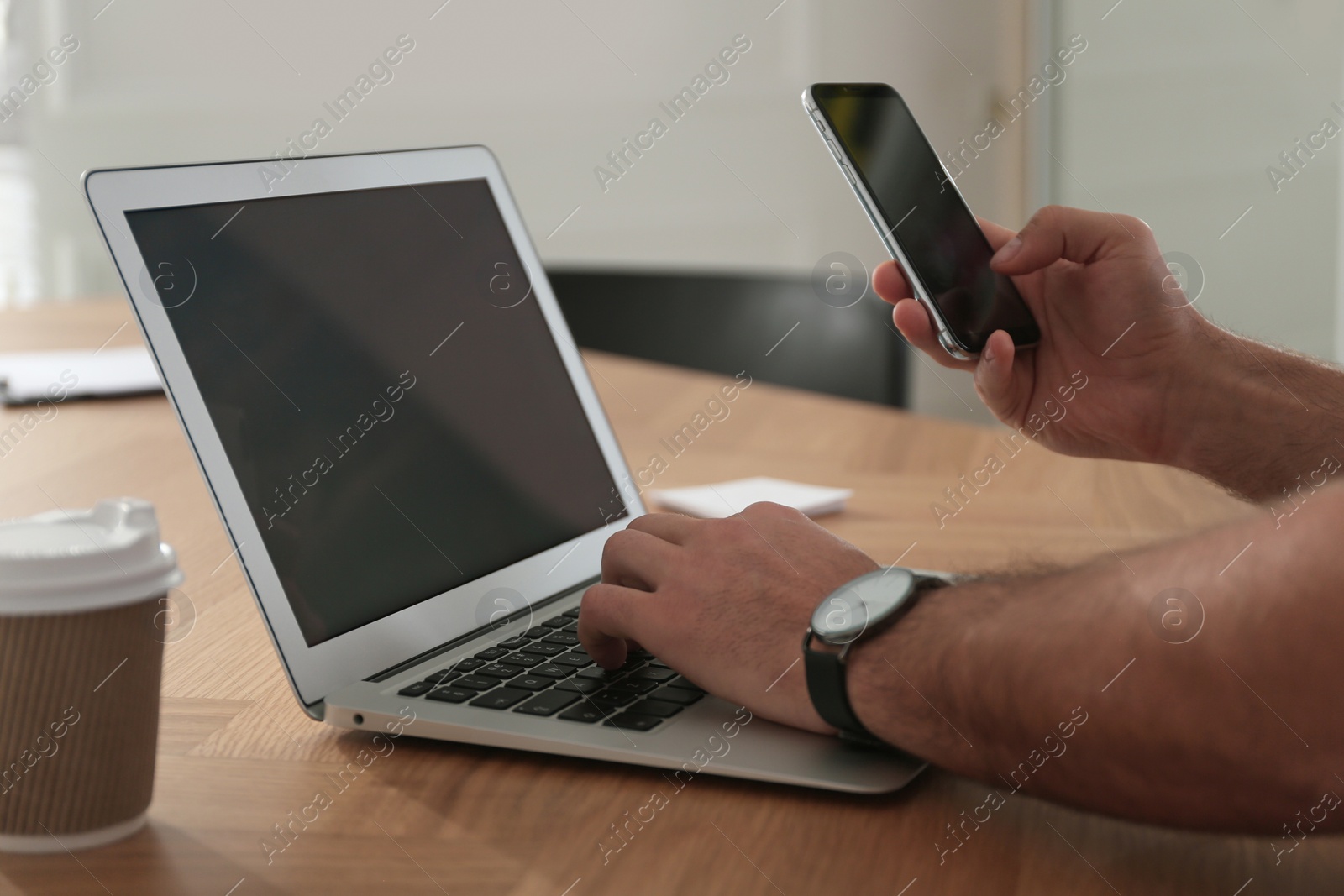 Photo of Freelancer working with laptop and smartphone at table indoors, closeup