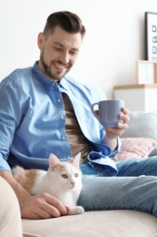 Photo of Young man with cute cat on sofa at home