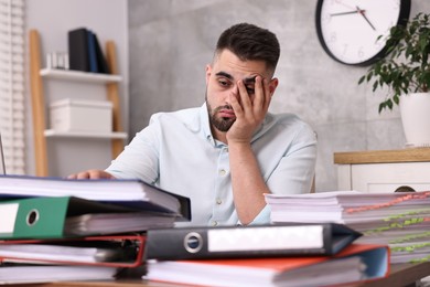 Photo of Overwhelmed man surrounded by documents at workplace in office