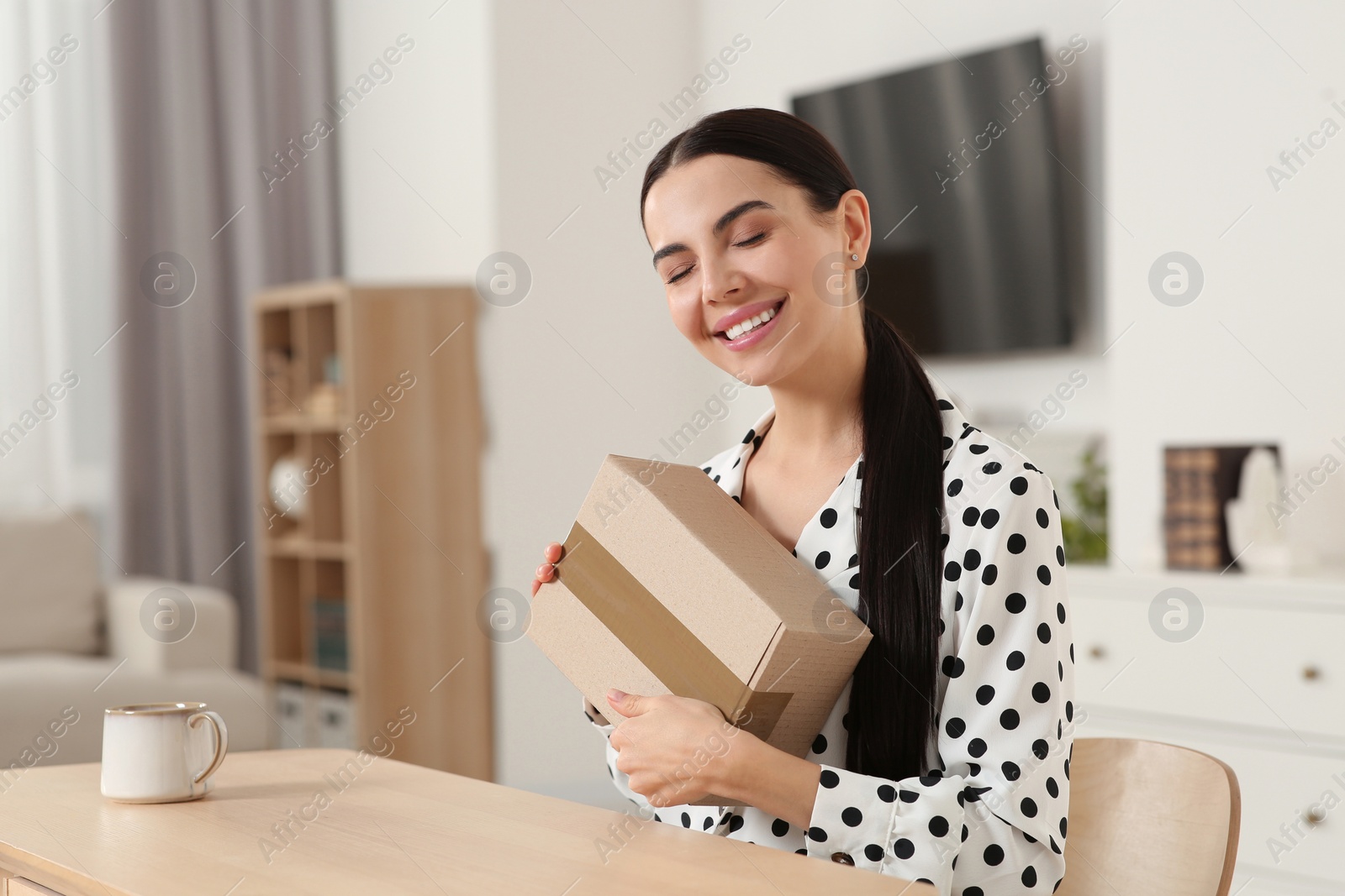 Photo of Happy young woman with parcel at table indoors. Internet shopping