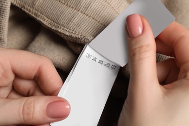 Woman holding clothing labels on beige garment, closeup