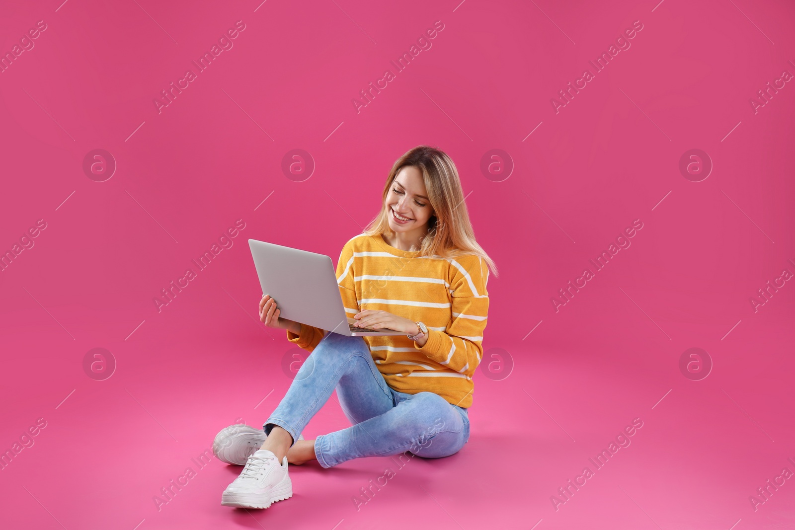 Photo of Young woman in casual outfit with laptop sitting on color background