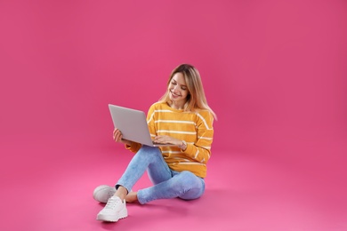 Photo of Young woman in casual outfit with laptop sitting on color background