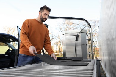 Photo of Man with auto carpets near vacuum cleaner at self-service car wash