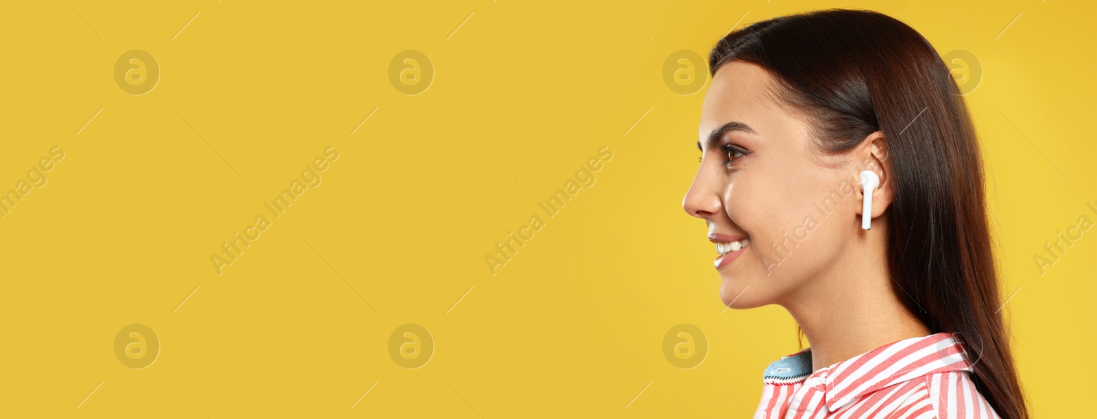 Image of Young woman listening to music with wireless earphones on yellow background, space for text. Banner design