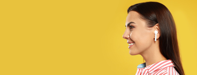 Image of Young woman listening to music with wireless earphones on yellow background, space for text. Banner design