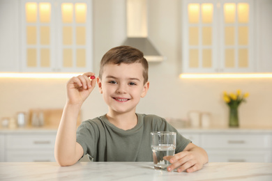 Photo of Little boy with glass of water and vitamin capsule in kitchen