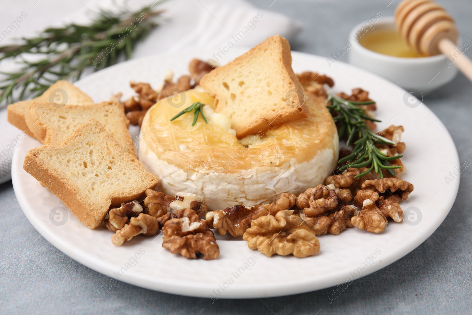 Photo of Tasty baked camembert, croutons, walnuts and rosemary on gray table, closeup