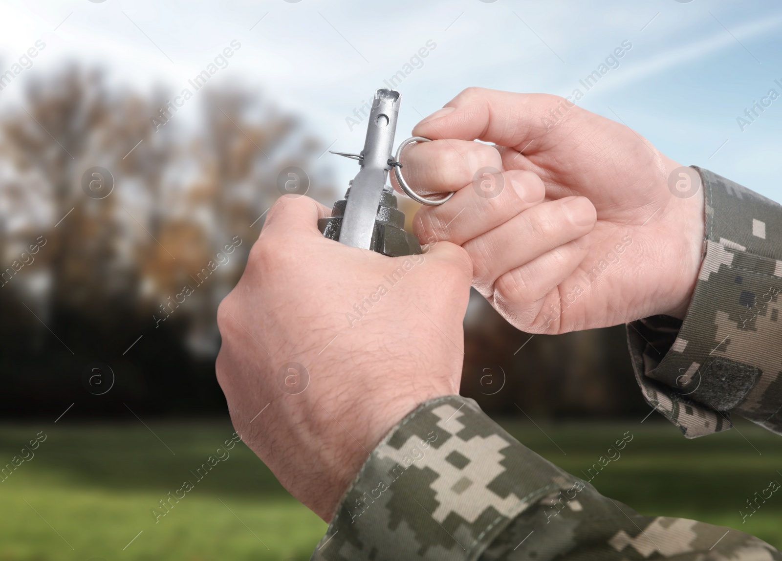 Image of Soldier pulling safety pin out of hand grenade outdoors, closeup